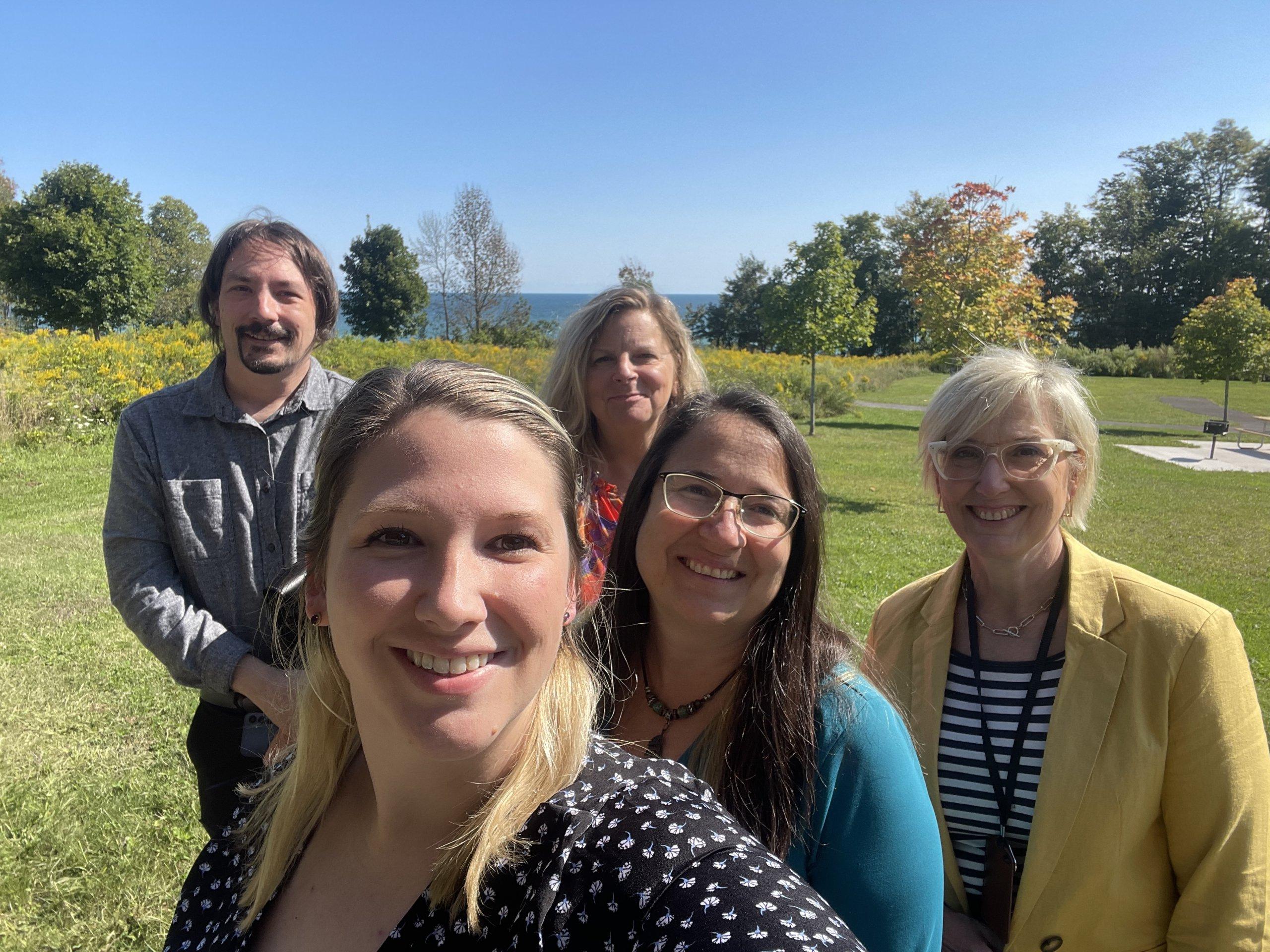 three women and one man standing outdoors during the Sumer with green trees behind them-Tour Cayuga Staff encourages you to contact them to help plan your visit.
